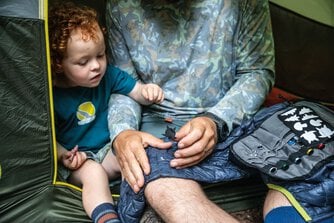 テントの中でウェアの補修作業を行う父と、その様子を見守る息子